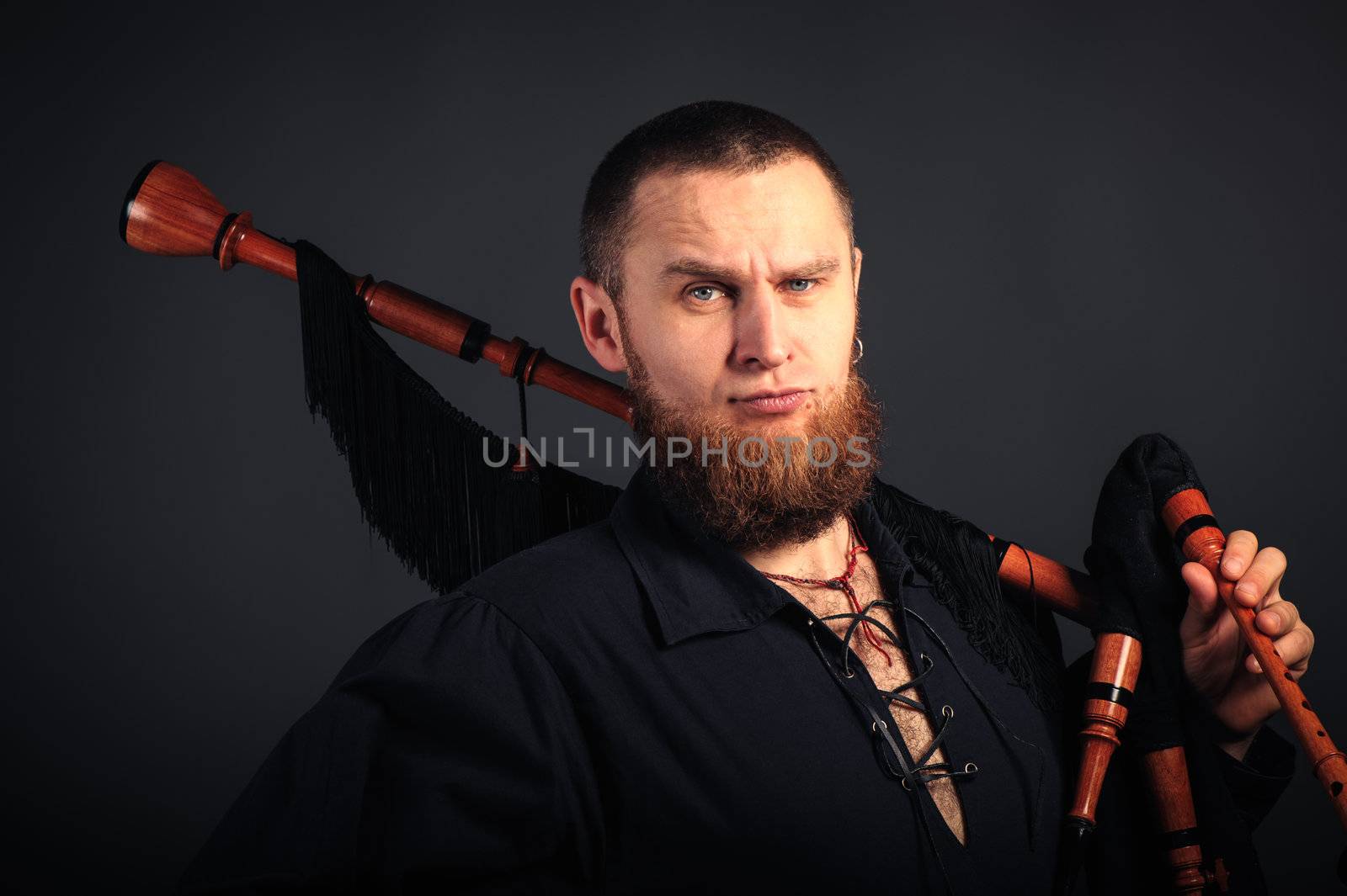 Young man with beard in scottish costume with pipe in his hand. Studio shot