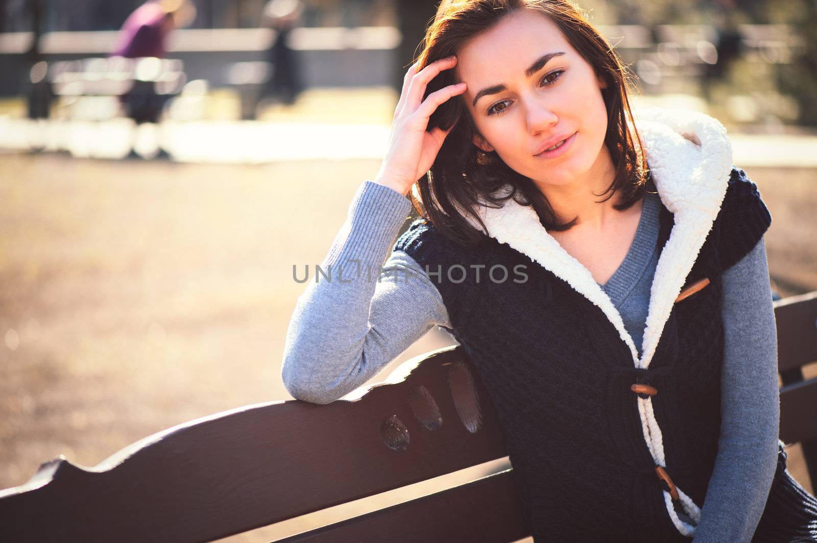 Portrait of young girl sitting on a bench in spring park in sunny day
