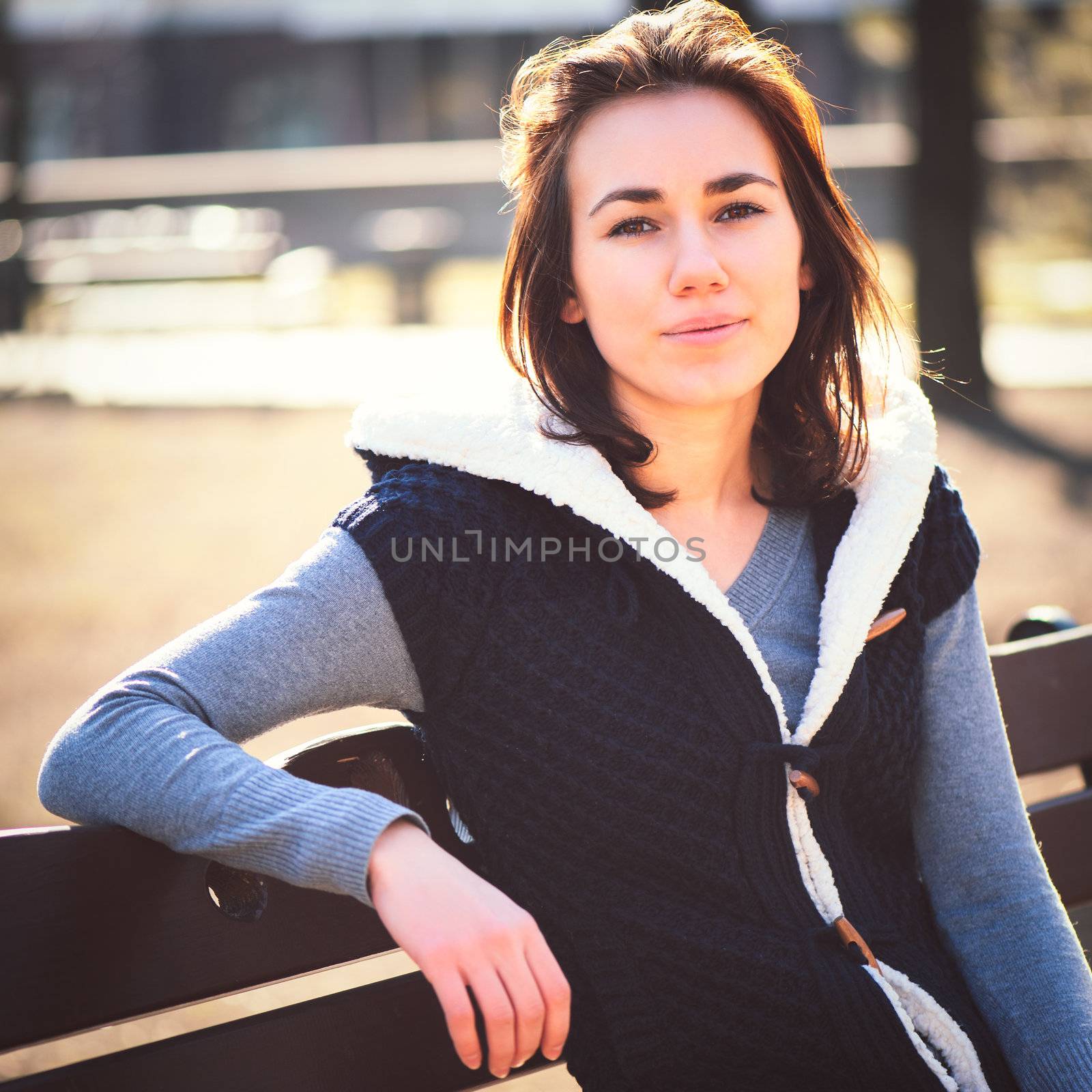 Portrait of young girl sitting on a bench in spring park in sunny day