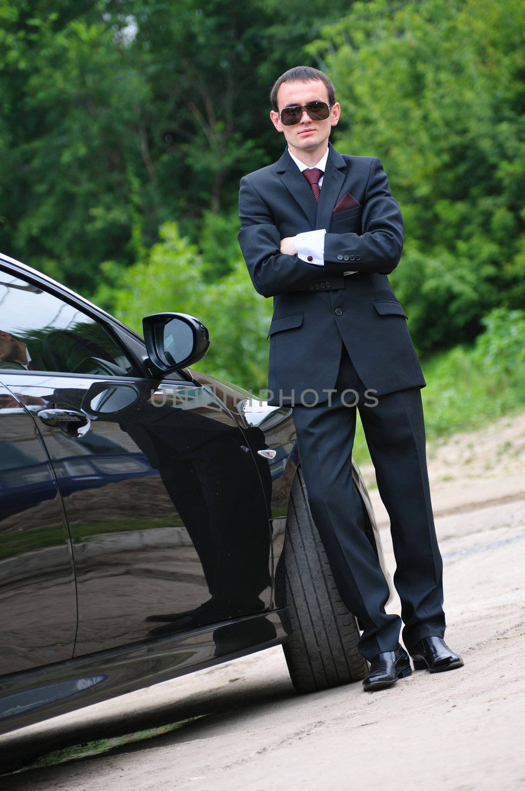 The young man with black glasses and suit stand near to expensive car