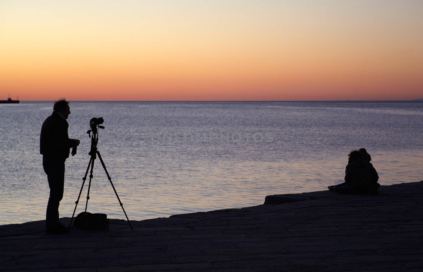 Photographer with camera and tripod take a picture at sunset