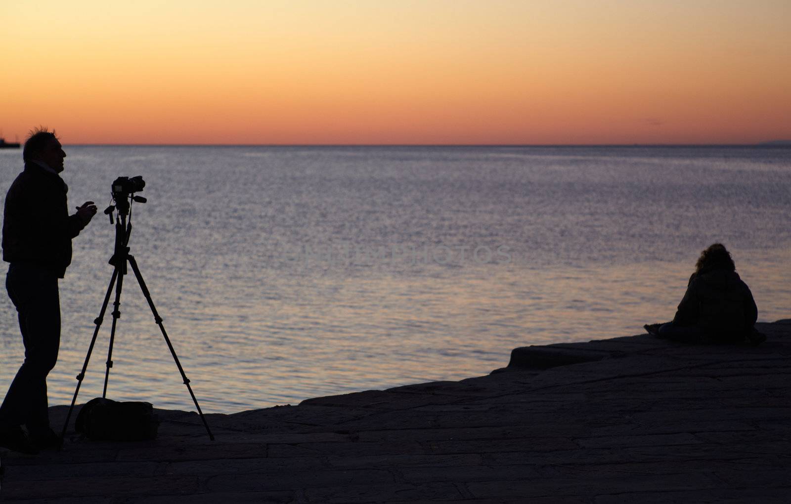 Photographer with camera and tripod take a picture at sunset