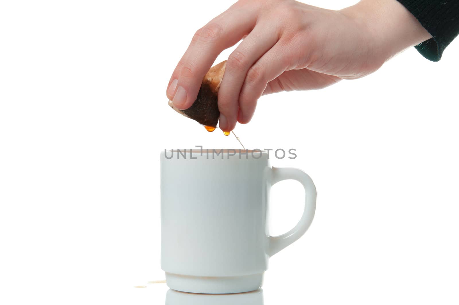 Hand wringing out tea bag in a mug on white background