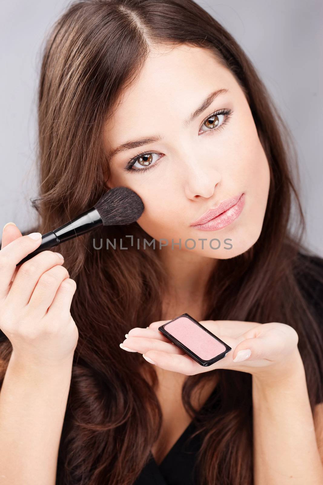 pretty young woman doing make up with powder brush