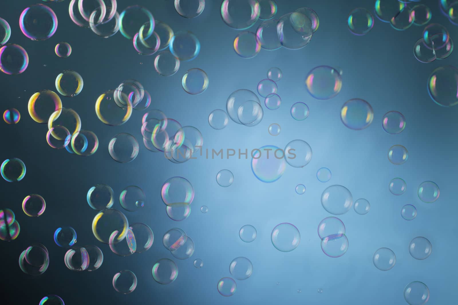 Real soap bubbles floating mid-air over blue background.