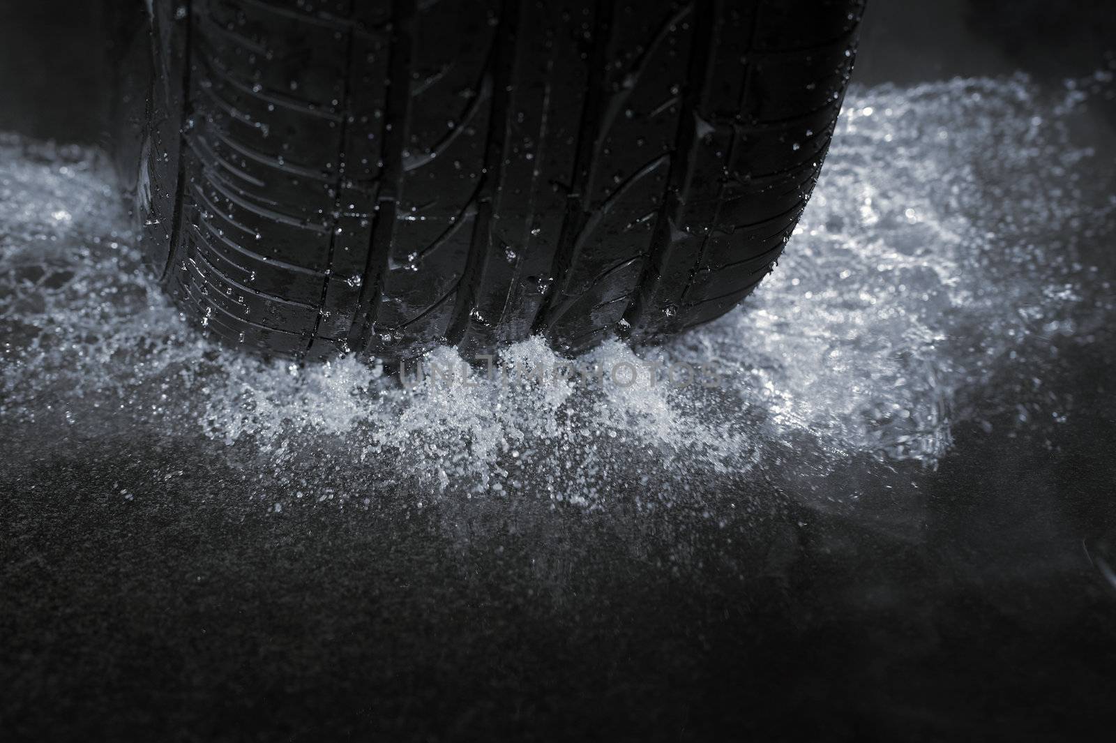 A Car tire on a wet road. The rain groove is a design element of the tread pattern specifically arranged to channel water away from the footprint.