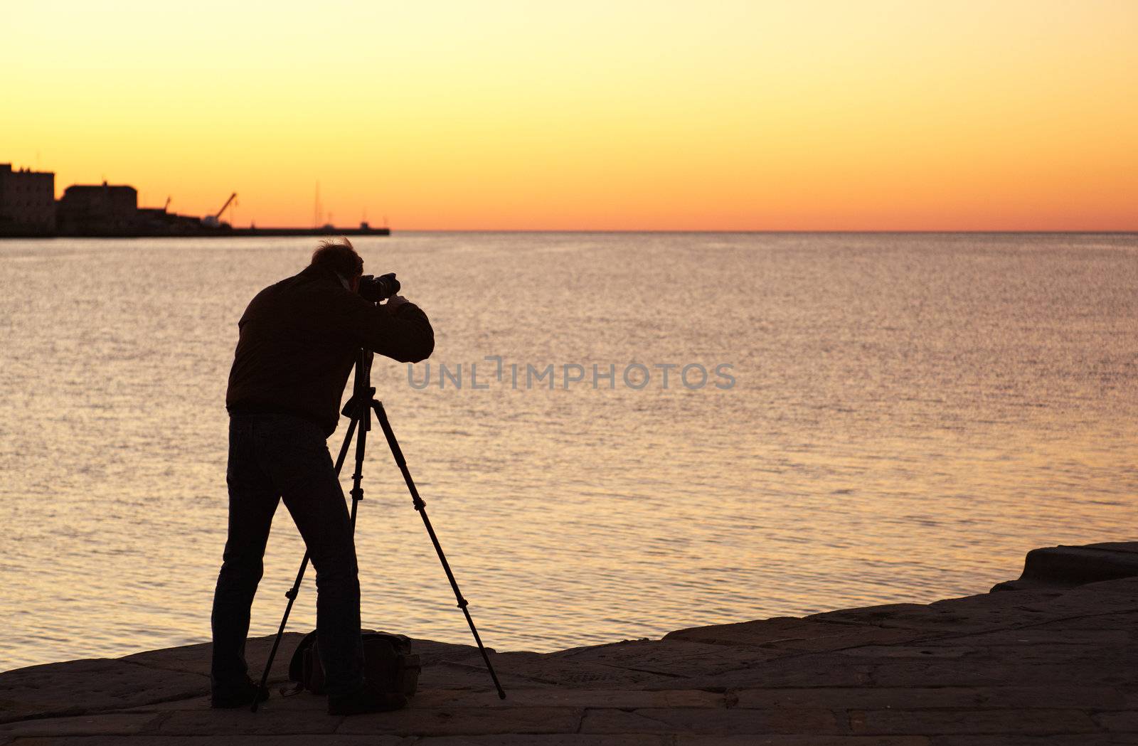 Photographer with camera and tripod take a picture at sunset