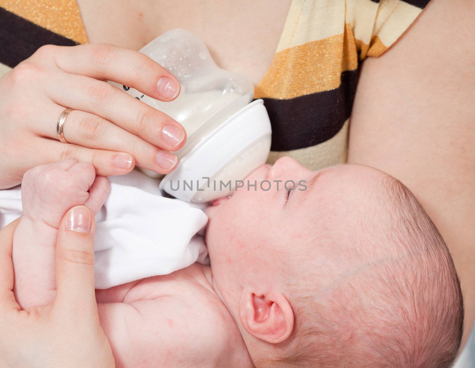 Mother feeds the baby with milk from a children's small bottle