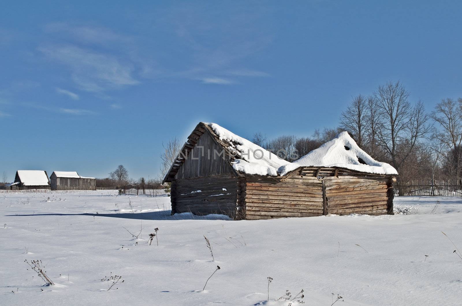 Old wooden barn with a snow-covered sagging roof, winter sunny day