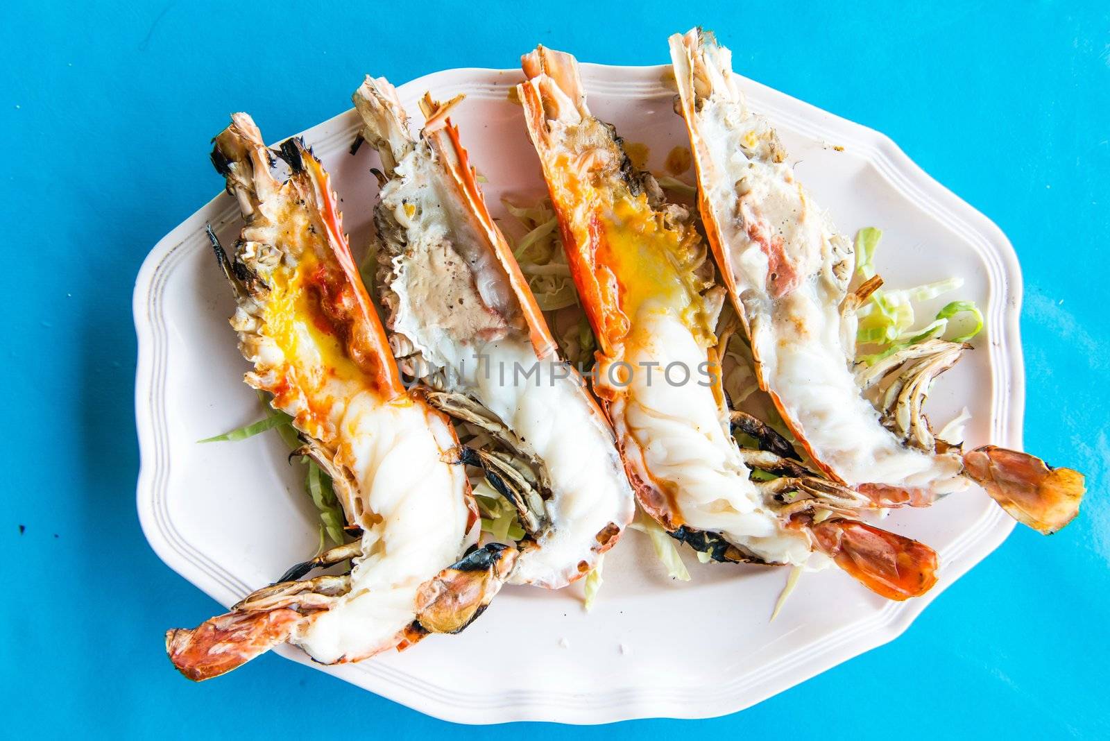 Grill river prawns on a plate with blue background, cut in half and expose its meat