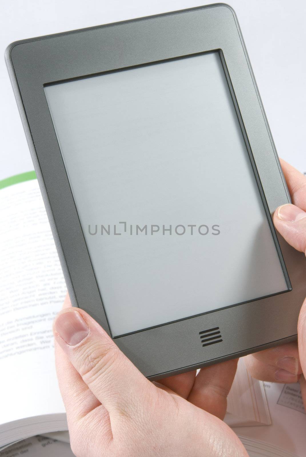 Man hands holding  an electronic book reader with blank screen, open books in the background