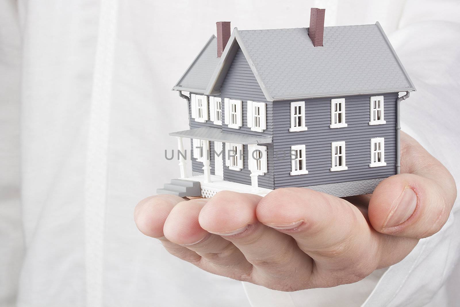 Close-up photograph of a miniature house in a man's hand.