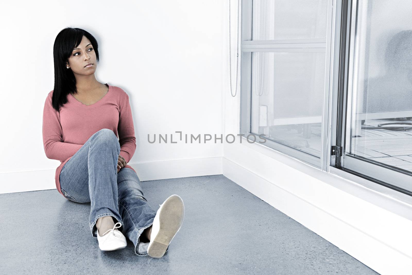 Depressed black woman sitting against wall looking out window