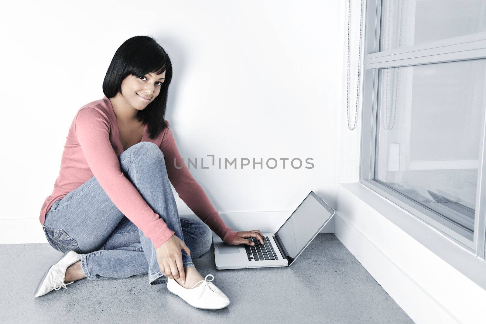 Young black woman with laptop computer sitting on floor smiling