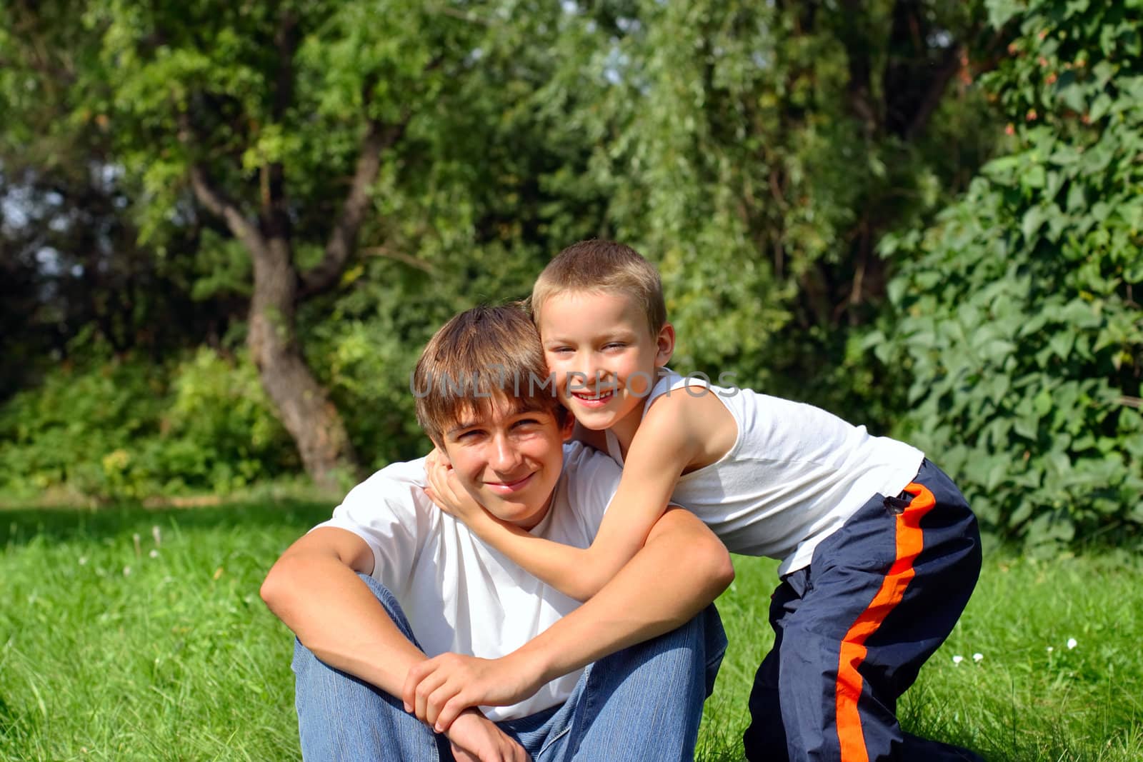 Happy little brother embrace his older brother in the summer park