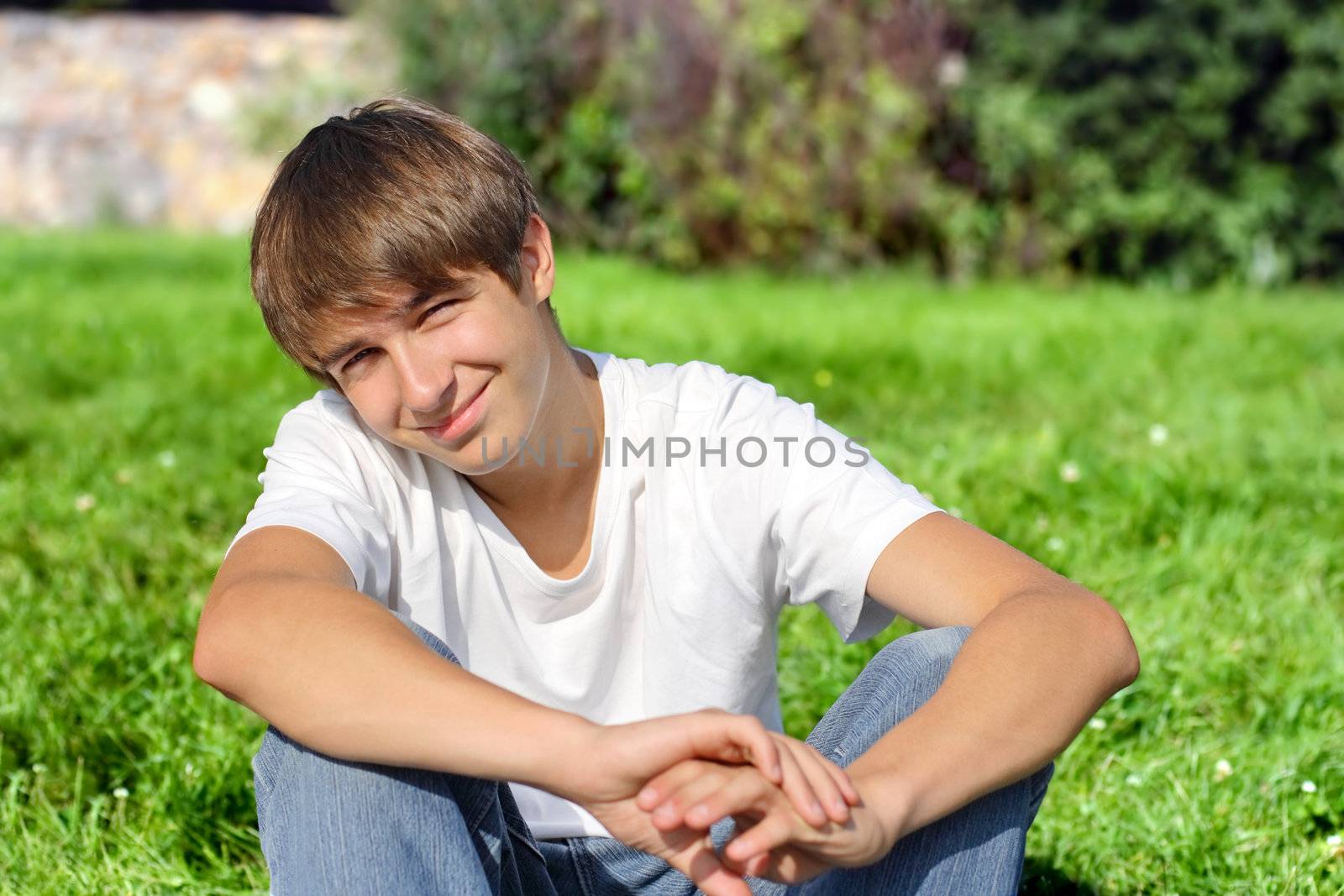 Happy Teenager sit on the Grass in the Summer Park