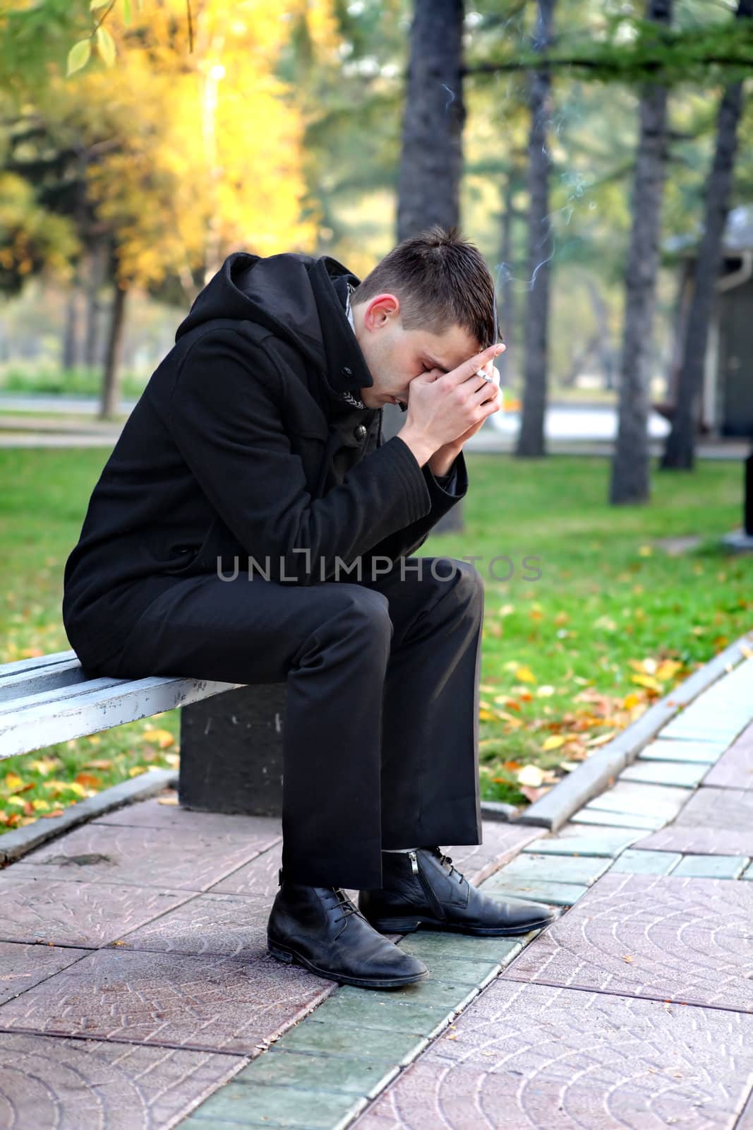 Sorrowful man sitting and smoking on the bench in the autumn park