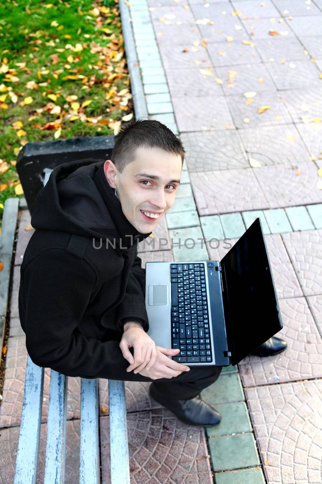 Happy Young man with Laptop sitting on the bench at the Autumn Park