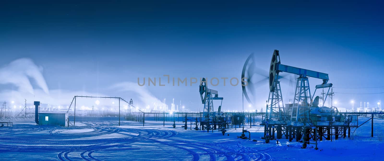 Oil and gas industry. Panoramic of a pumpjack and oil refinery in the winter with snow. Night view.