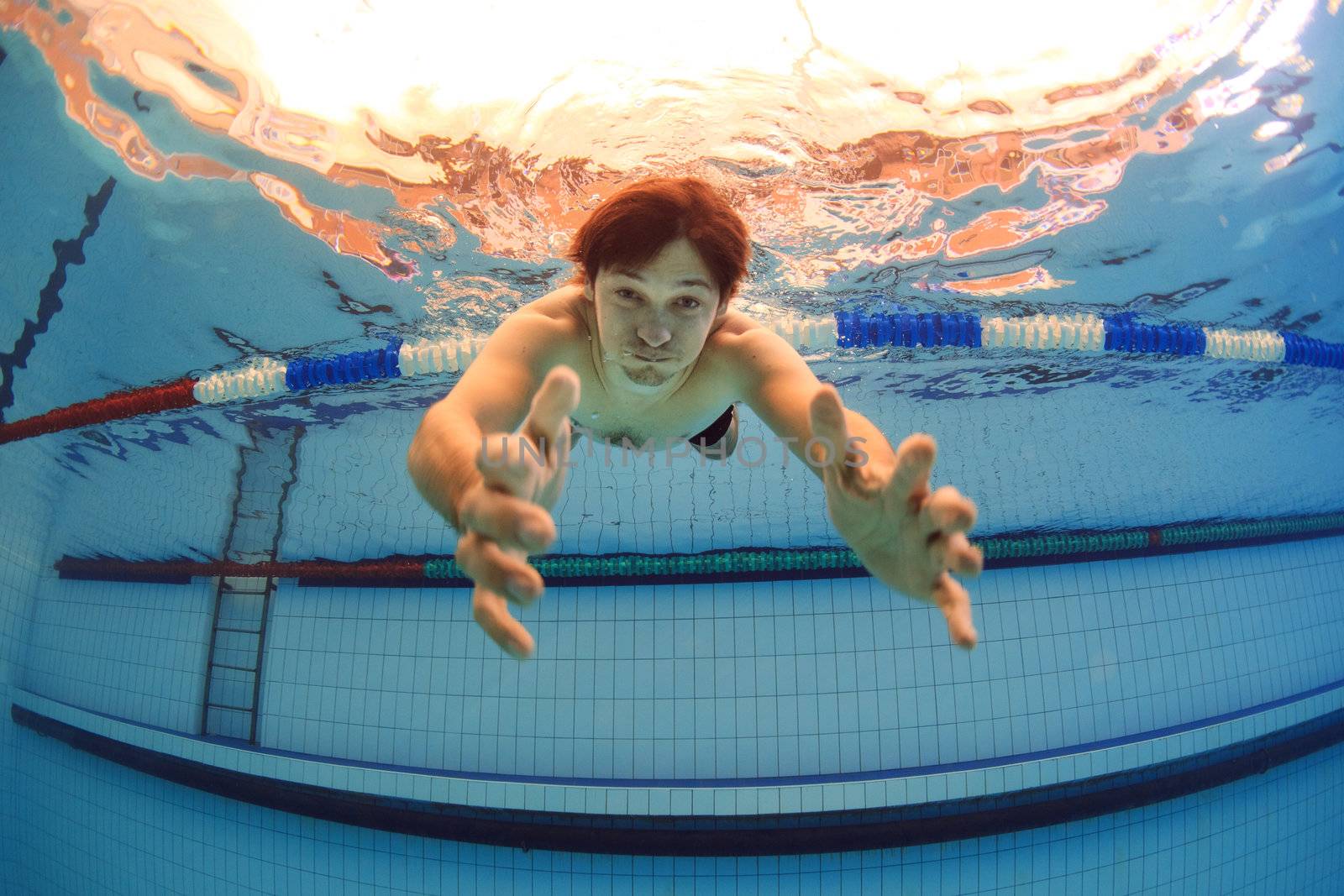 man underwater in swimming pool streching hands