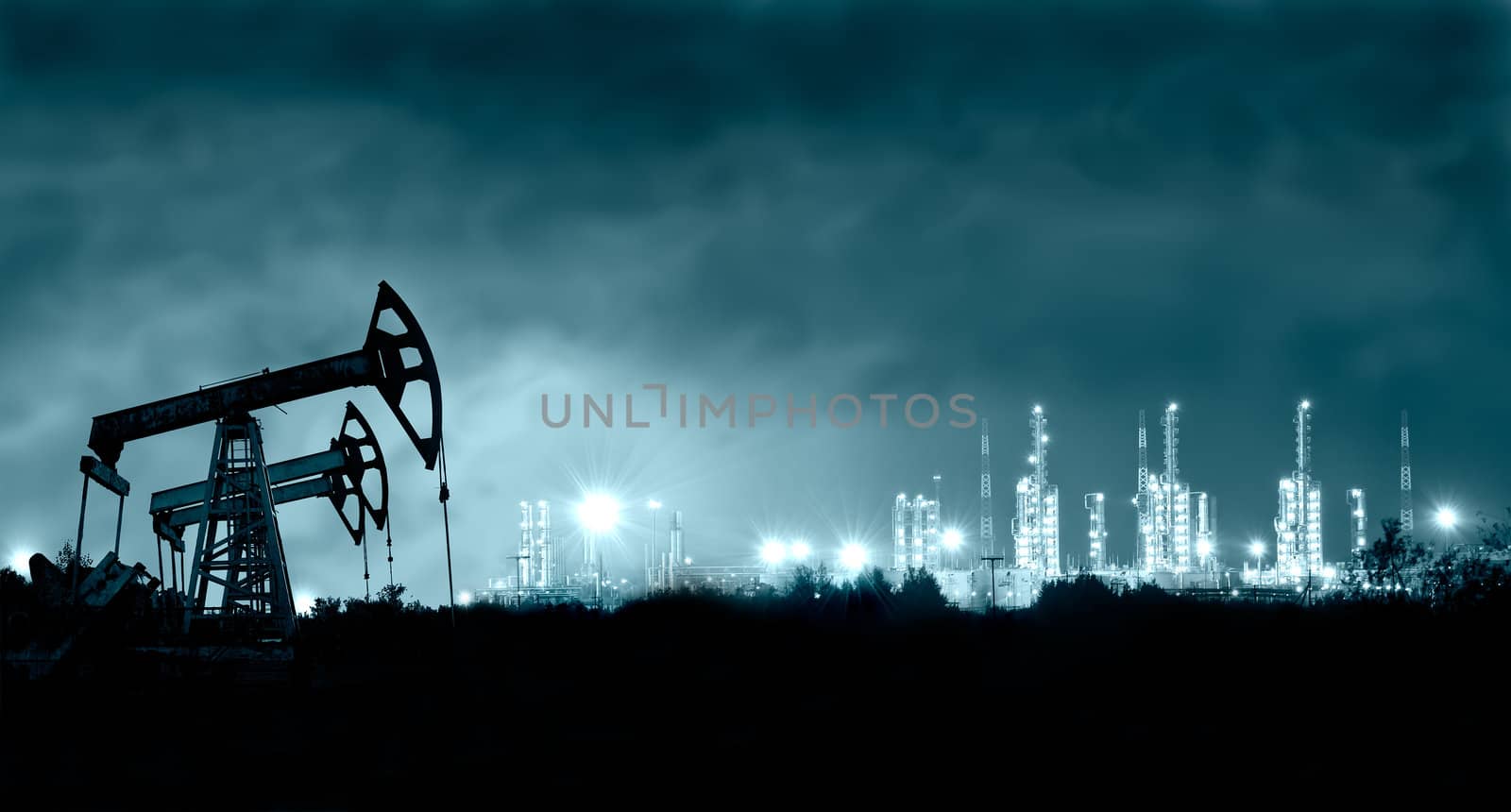 Group oil rigs and brightly lit industrial site at night. Toned.