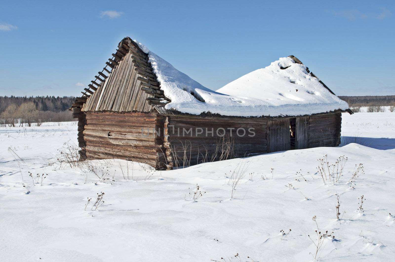 Old wooden barn with a snow-covered sagging roof, winter sunny day