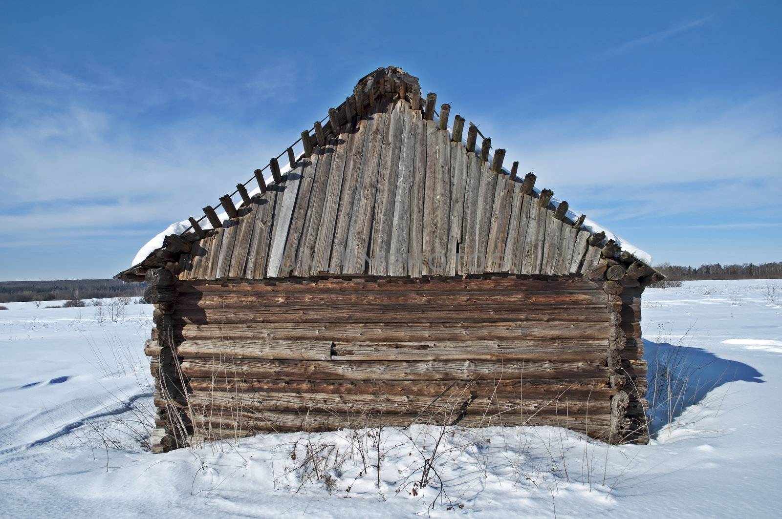 Old wooden barn on a snowy field, winter sunny day