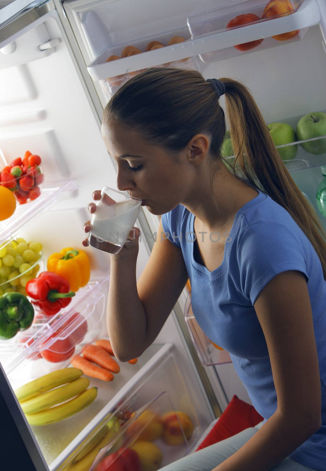 Young woman drinking milk near refrigerator at night