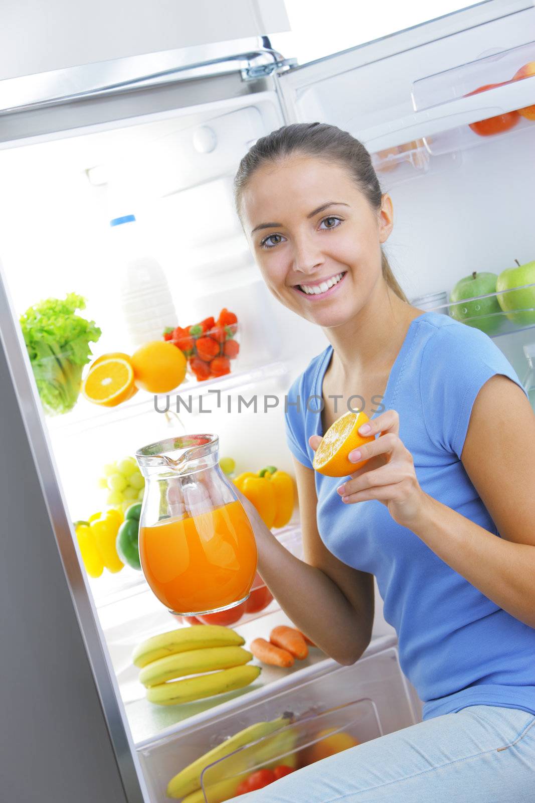 Beautiful young woman near refrigerator with a carafe of orange juice
