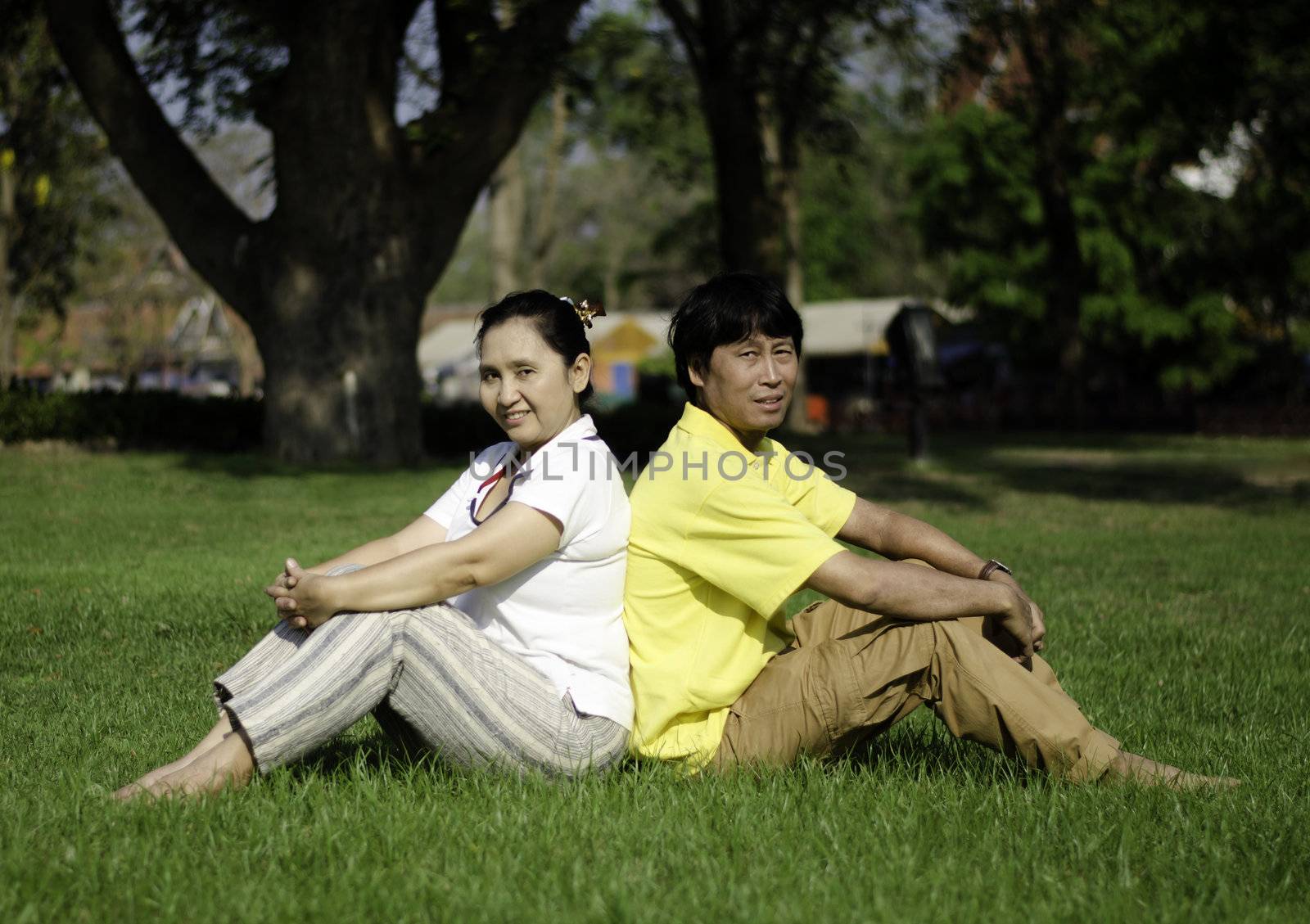Portrait of beautiful couple sitting on ground in park by siraanamwong