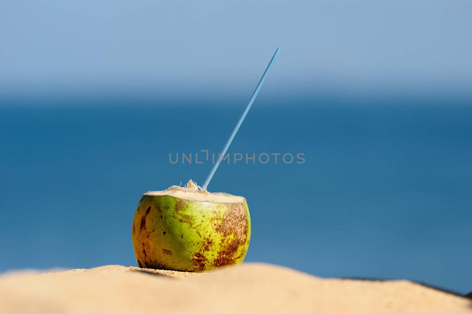 Coconut with drinking straw on the sand at the sea
