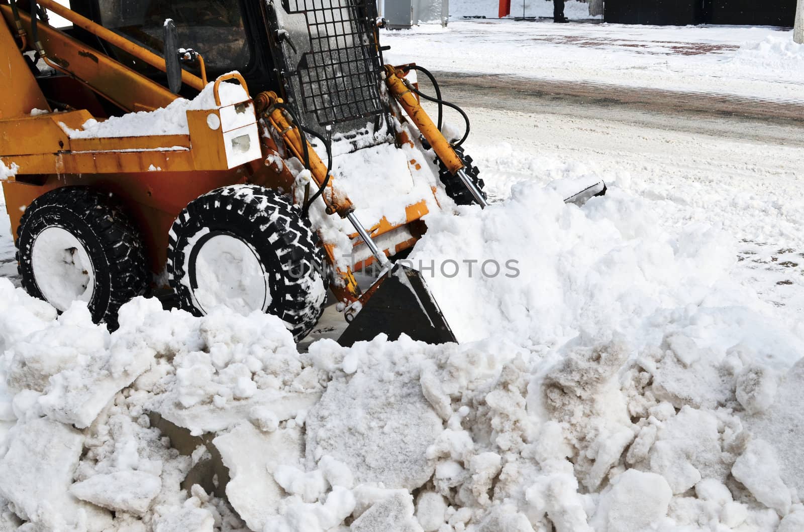 yellow tractor cleaning the snow on a street