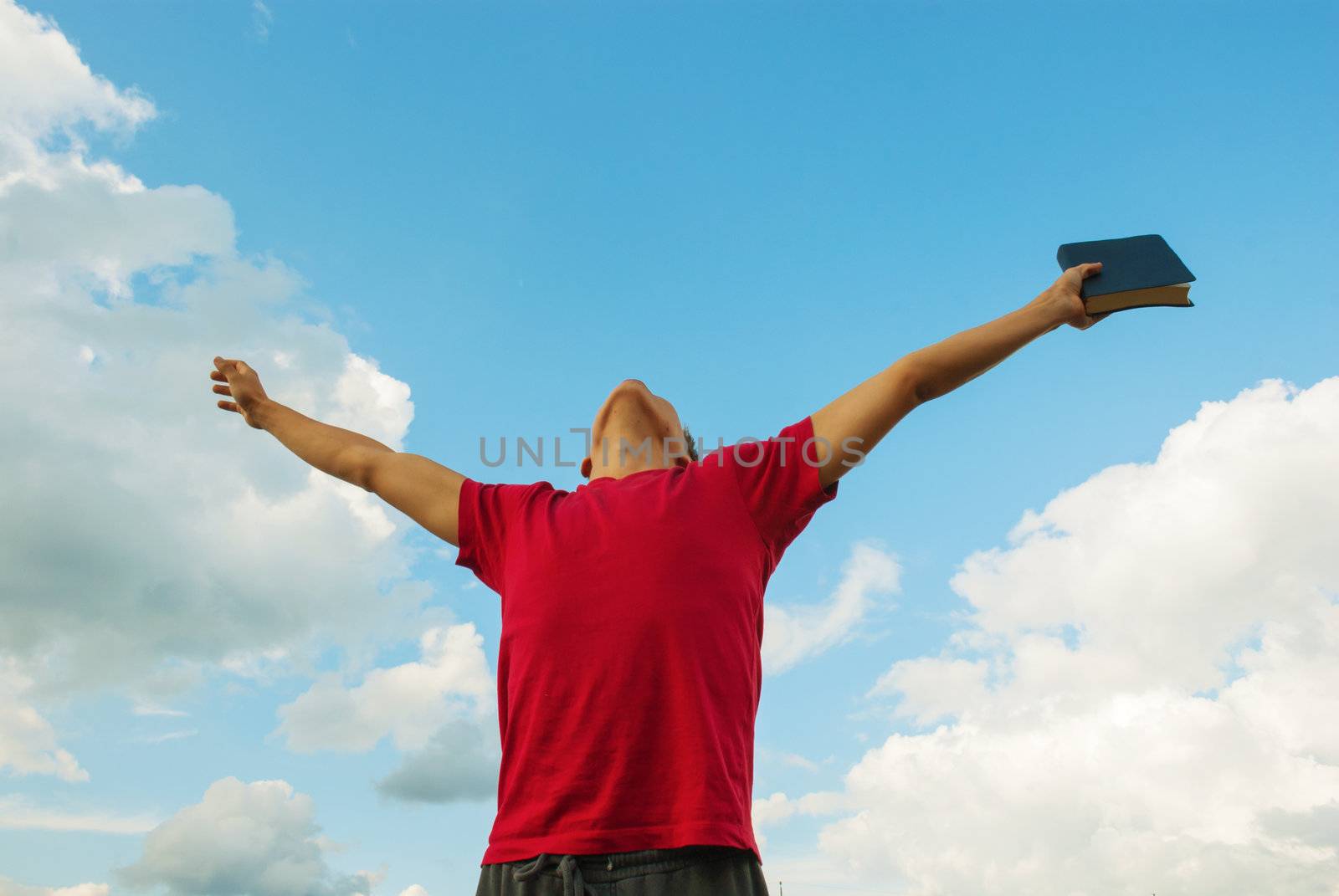 Young man staying with raised hands against blue sky