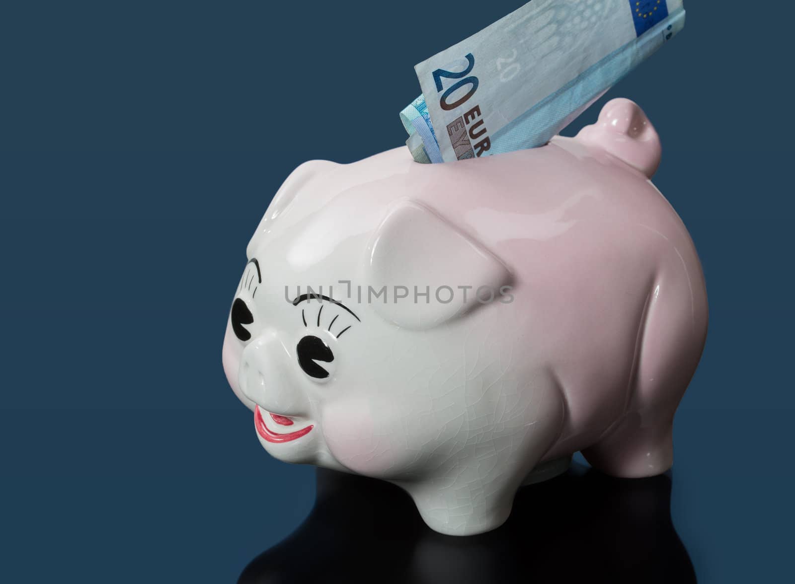 A single twenty euro bill inserted into the slot on a piggy bank with blue reflection