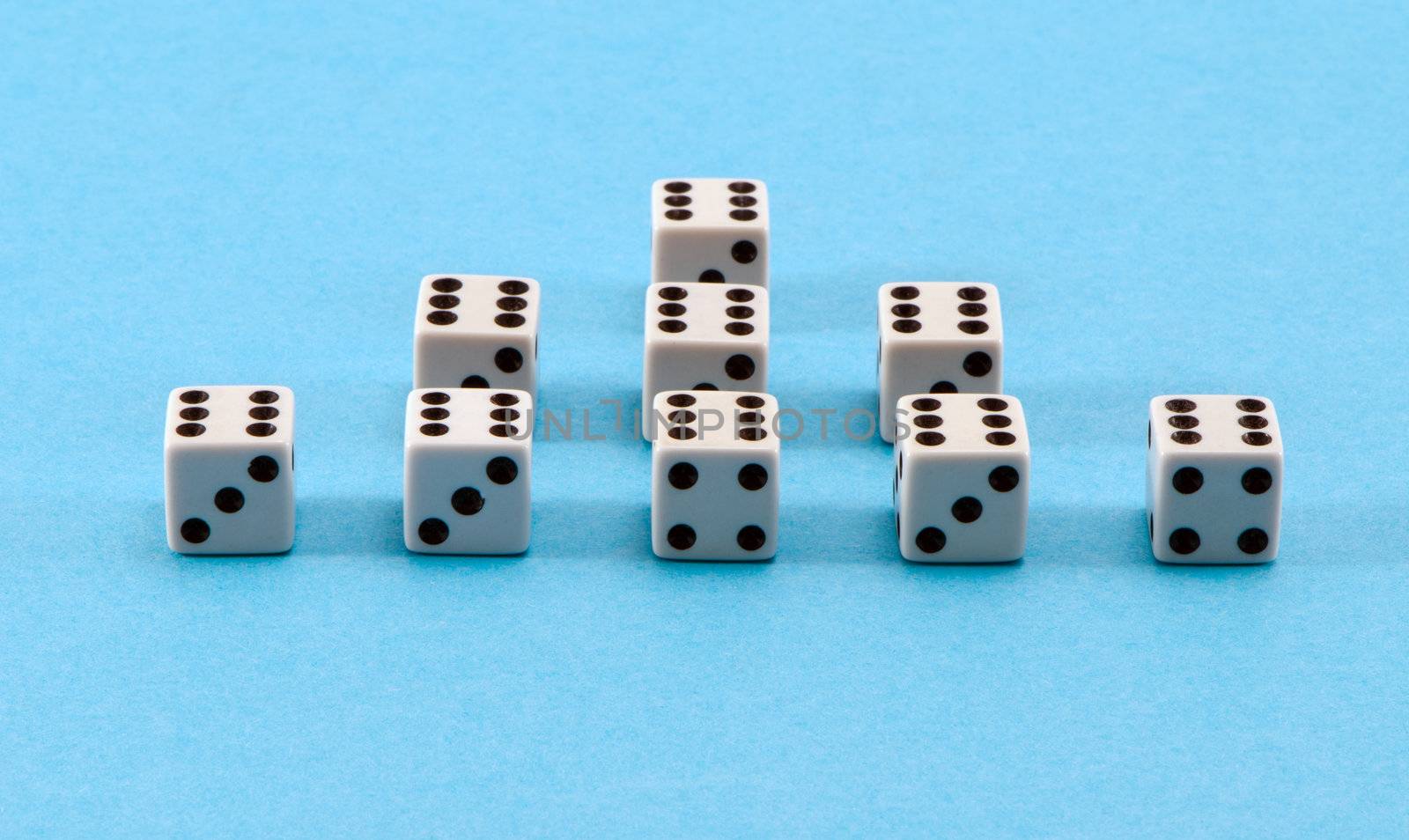 closeup of white gamble dice pyramid with six black dots on blue background.