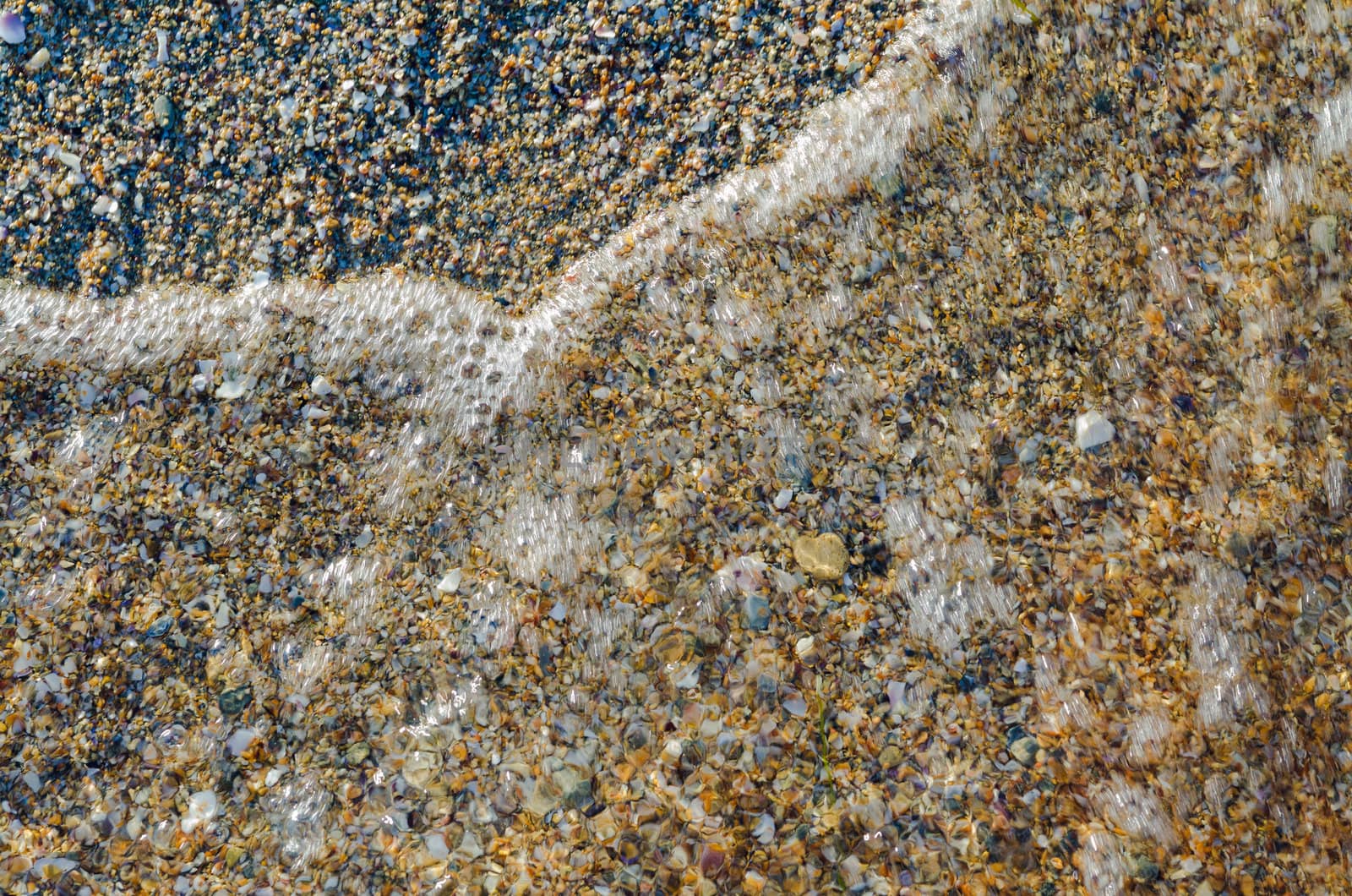 many small pebbles background on seashore. Motion transparent water wave