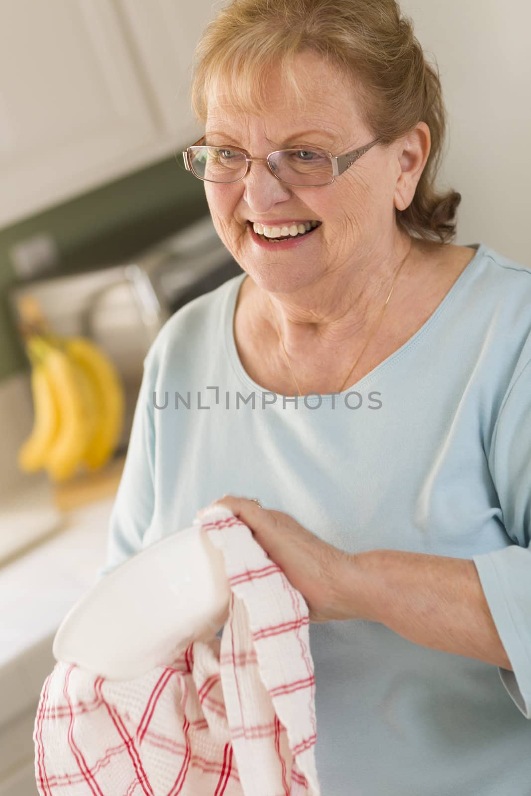 Senior Adult Woman Drying Bowl At Sink in Kitchen by Feverpitched