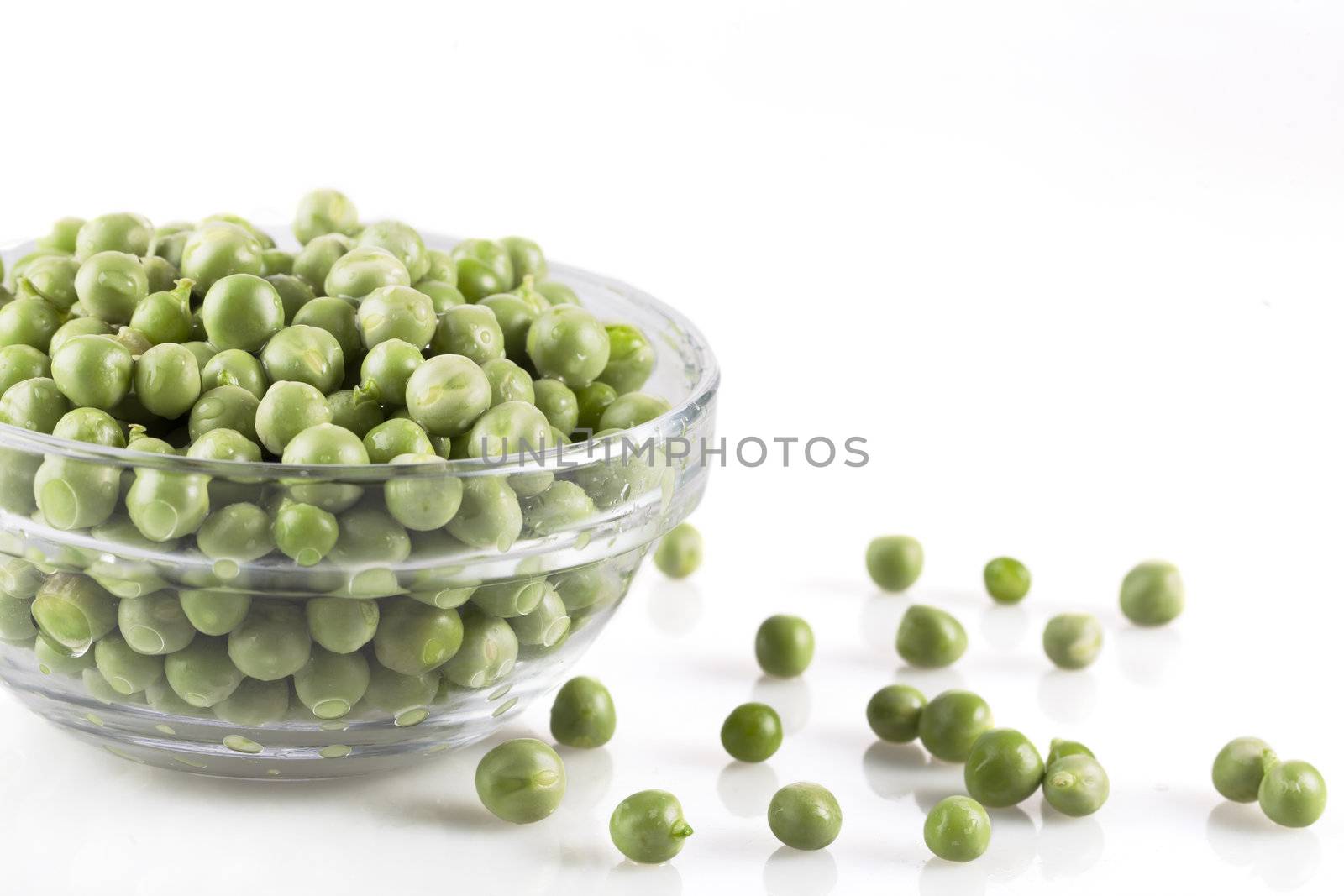 Fresh green peas in a glass bowl and on white surface.
