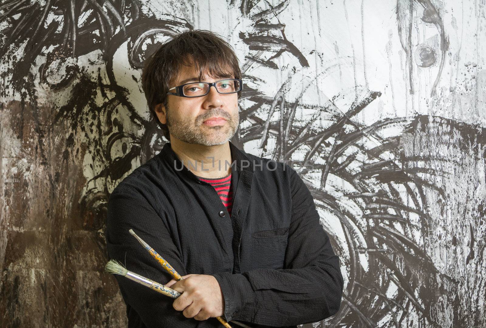 Painter artist with black glasses posing in front of his mural paint