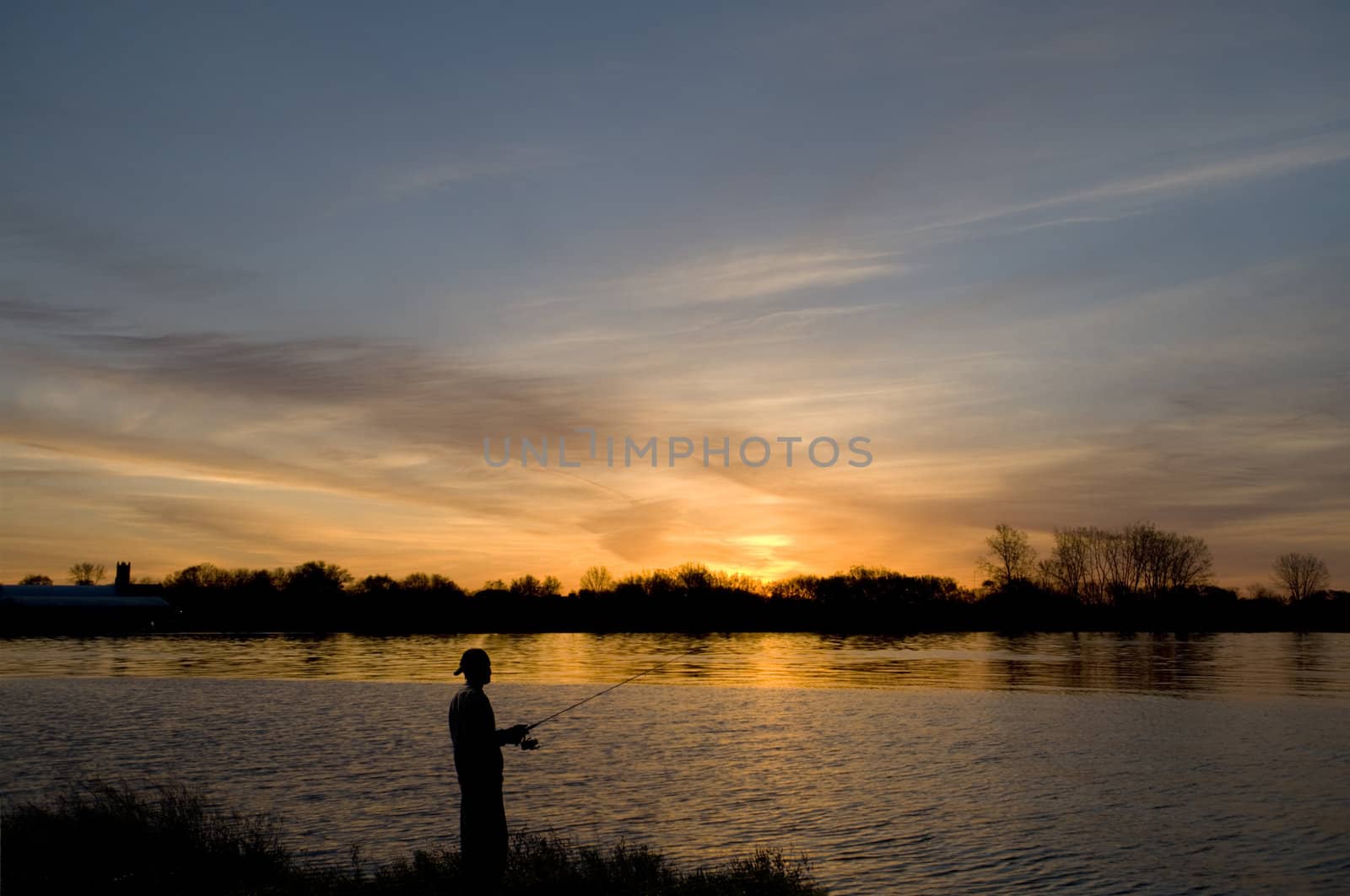 Man fishing from the river's edge at sunrise