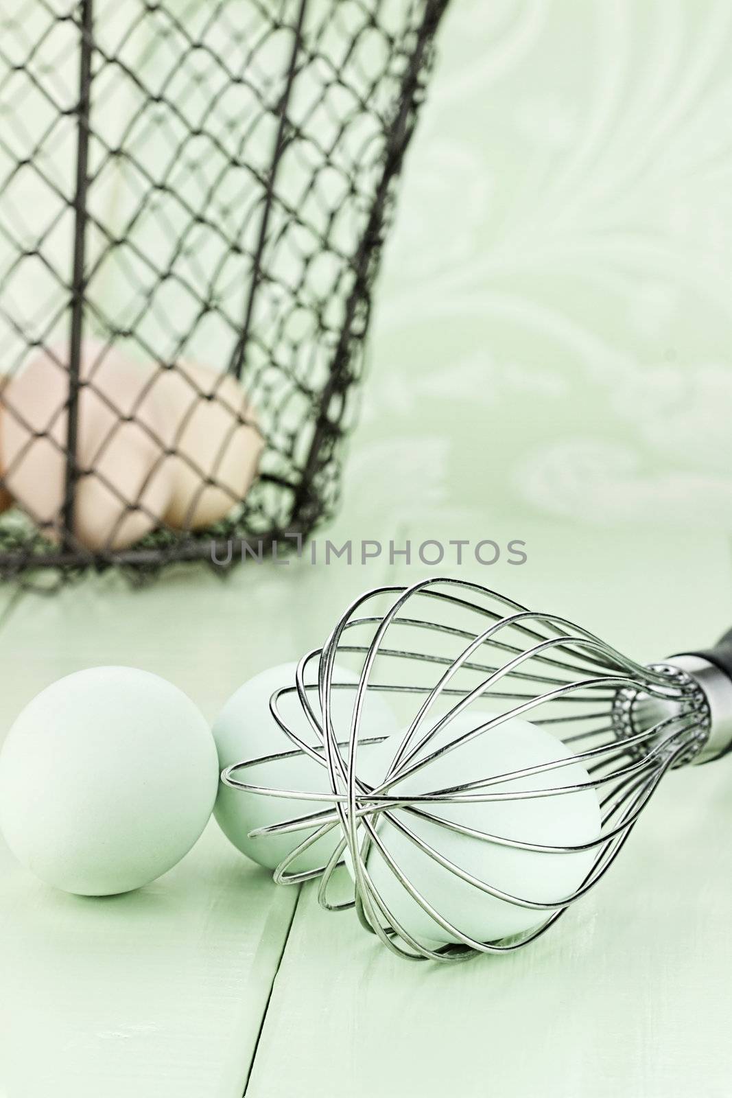 Fresh free range Ameraucana eggs in a whisk with brown eggs in a vintage basket in background. 
