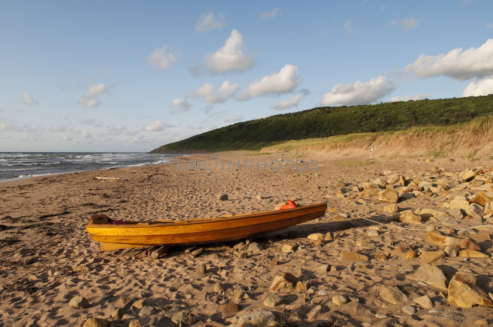 Wooden boat resting on the beach with the waves crashing in and the sun setting giving a golden colour in the scenic