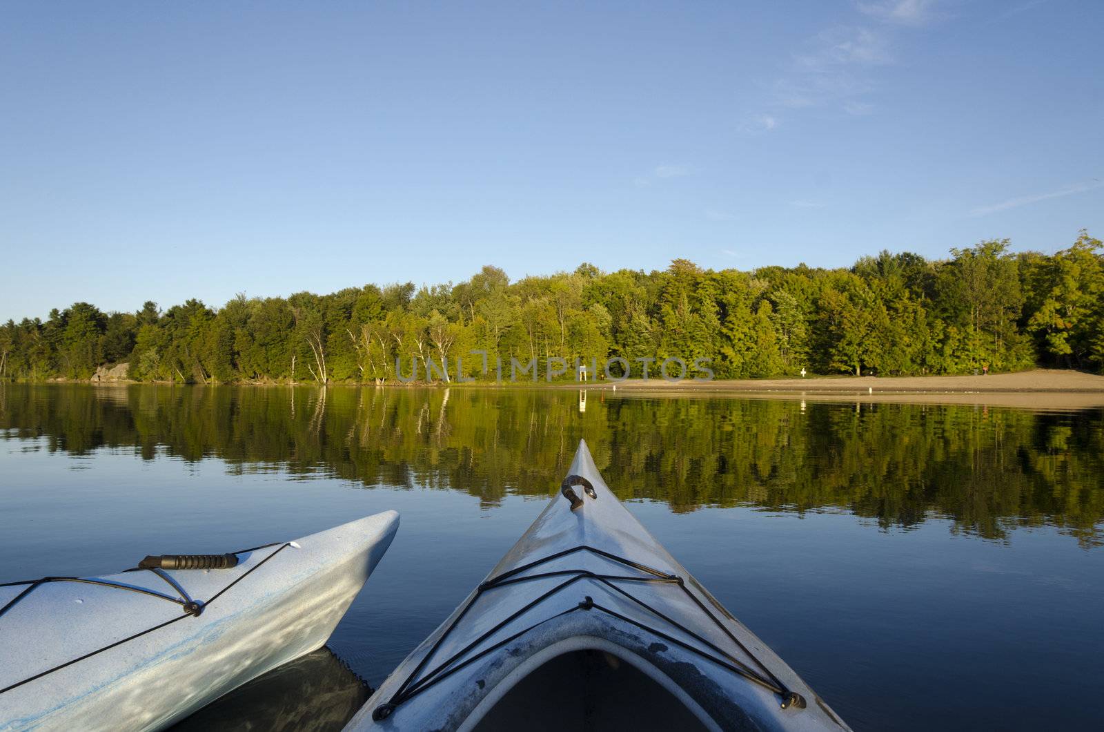 Two kayaks floating on calm Charleston Lake facing the beach with the evening light 