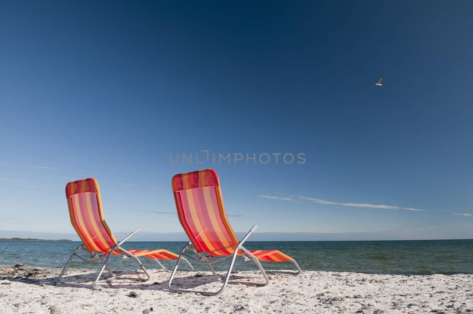 Lounging beach chairs on the Lake Ontario shoreline with large copy space area in the deep blue sky