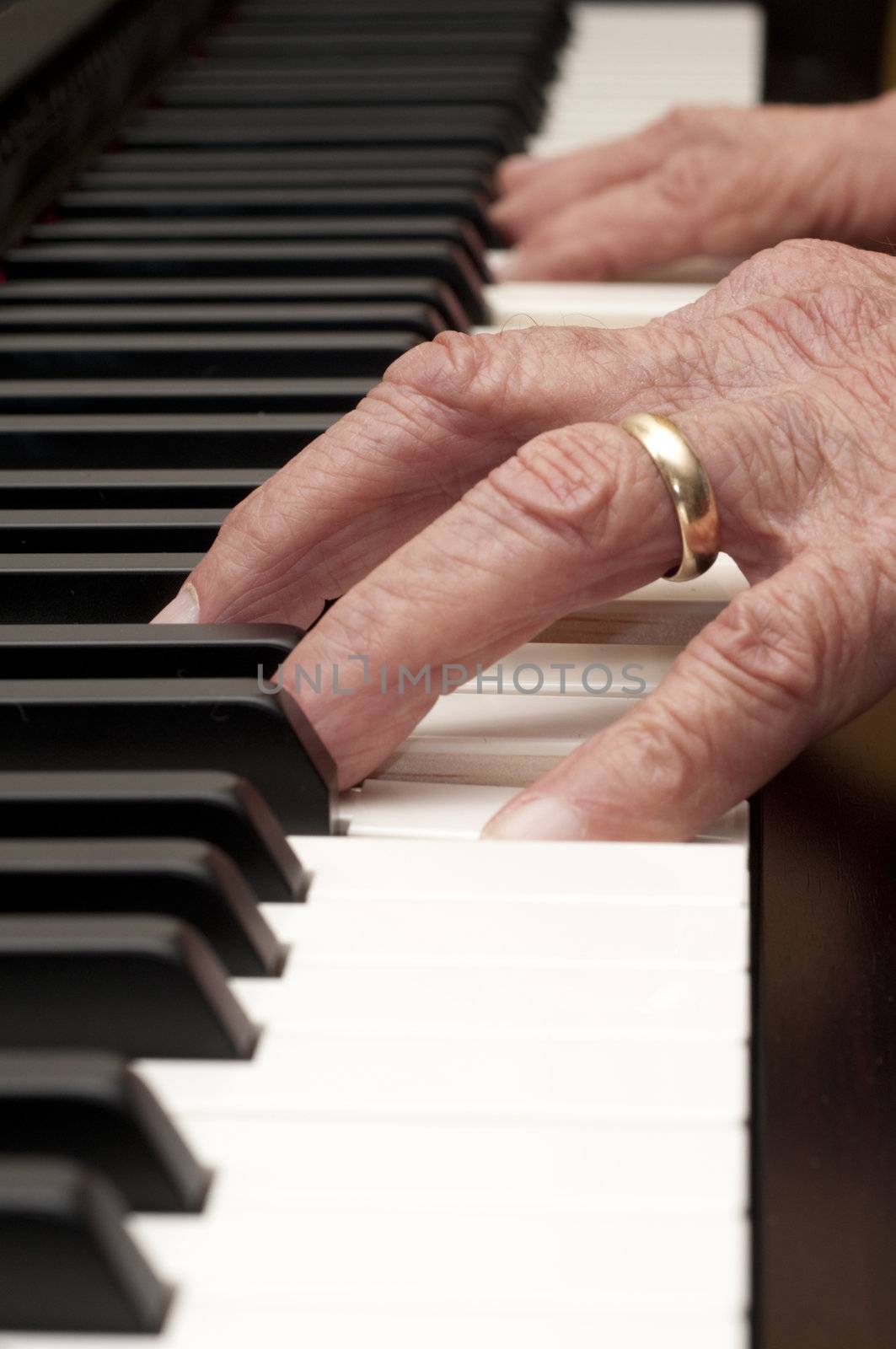 Selective focus on the foreground hand of an older man playing the piano