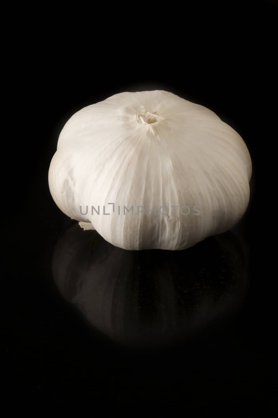 Garlic clove on black background with slight reflection on the tile