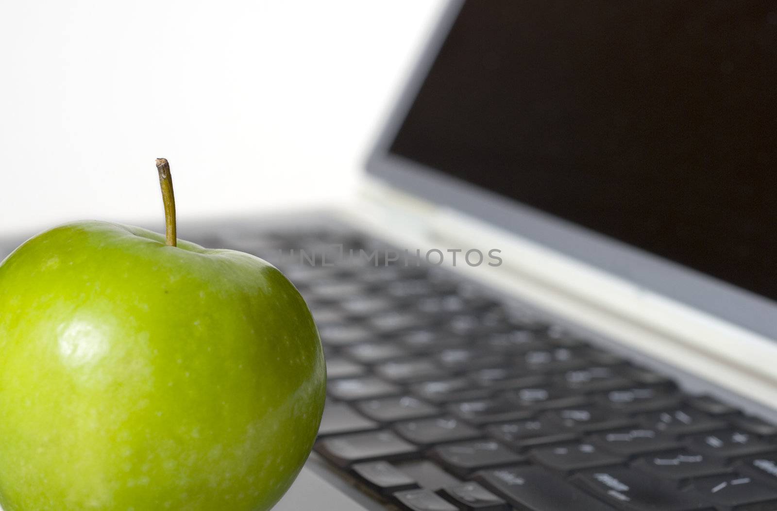 Macro shot with selective focus on green apple in the foreground with laptop in the background.