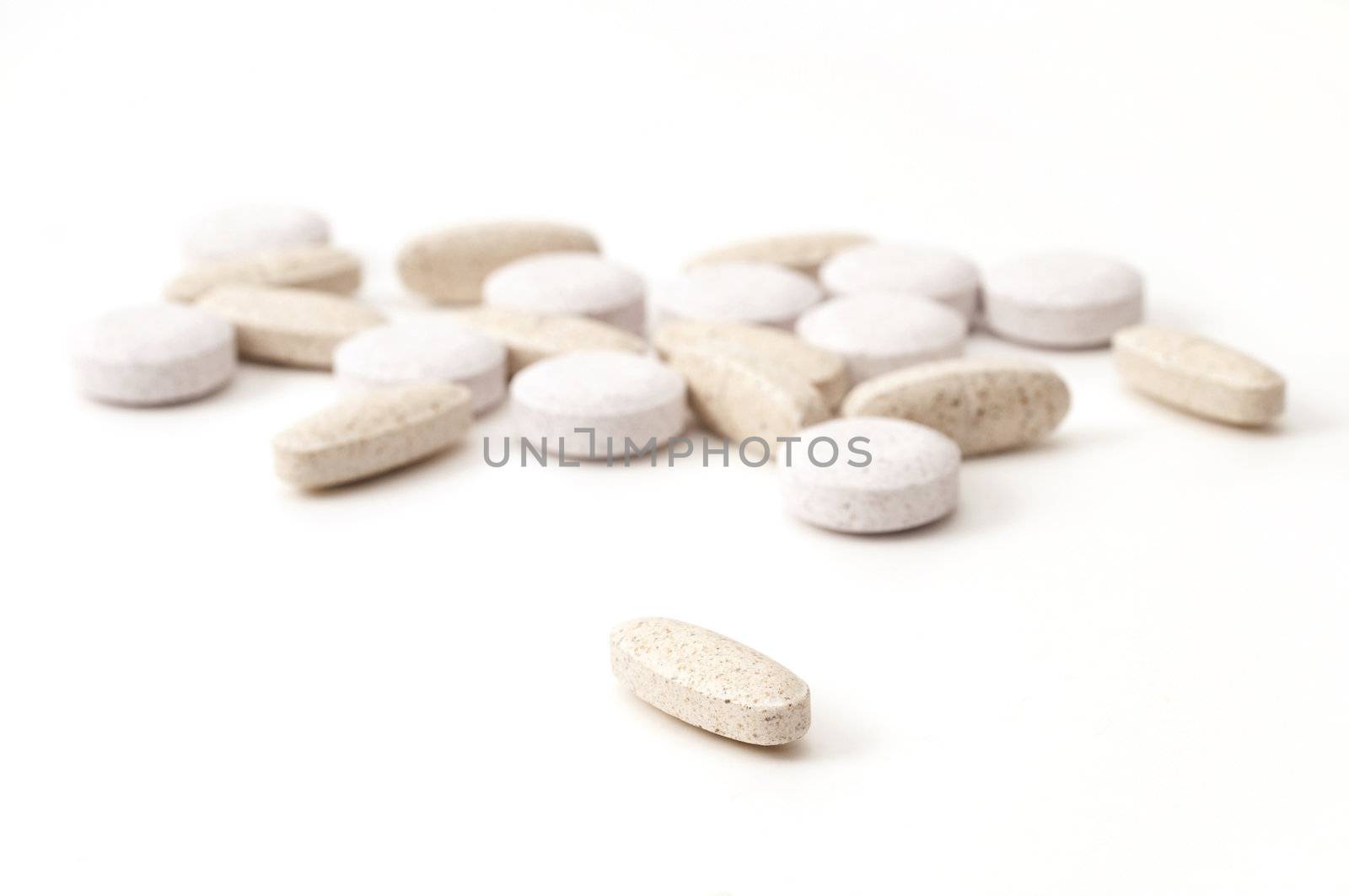 Selective focus on single multi-vitamin in the foreground with many vitamins in the background with soft focus isolated on white background