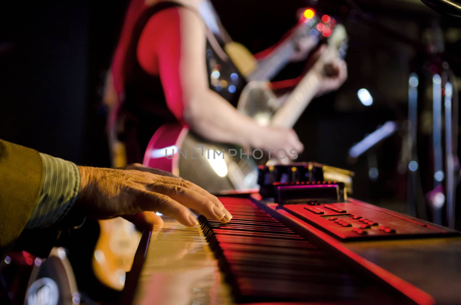 Selective focus on the hands on the keyboard at a blues festival with guitar players in the background