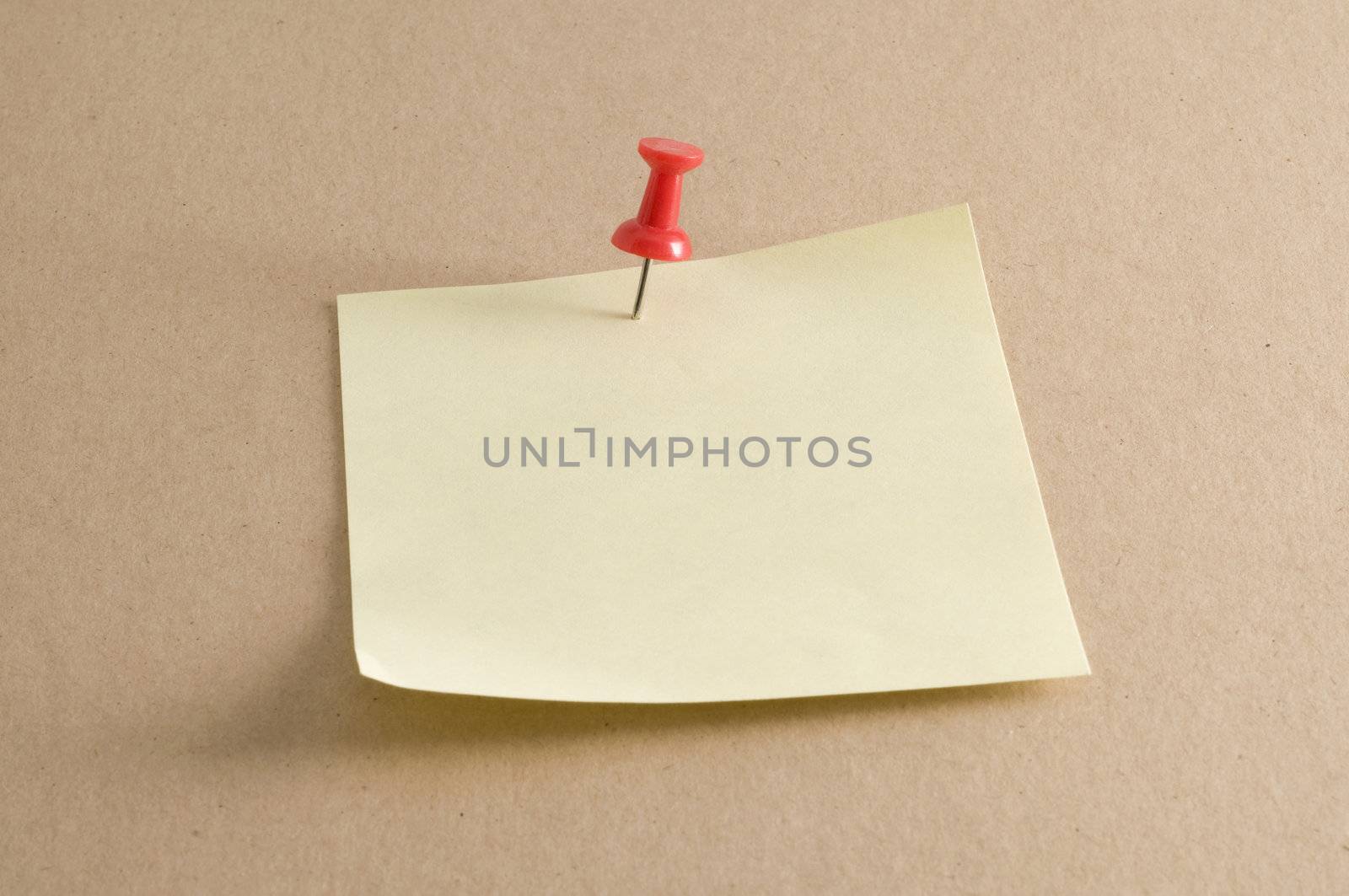 Macro of a pushpin holding a sticky note on a kraft folder